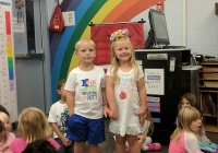 Two children posing in front of a colorful classroom backdrop on their first day of kindergarten.