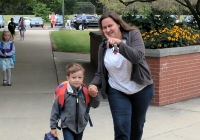 Woman and child walking down a sidewalk on first day of school.