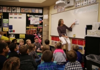 The teacher is standing in front of a whiteboard, instructing students on their first day of kindergarten.