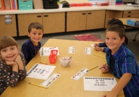 Children sitting at a table in a classroom, smiling and posing for a picture on their first day of kindergarten.