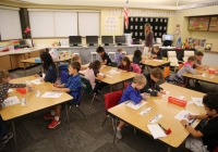 Children sitting at desks in a classroom, engaged in an activity on their first day of kindergarten.
