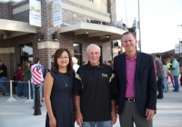 Three people standing in front of a building. The man on the left is wearing a blue shirt and glasses, the woman in the