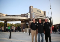 Three men posing in front of a stadium entrance sign.