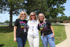 Three women posing in front of a school building on the last day of school, smiling and celebrating.