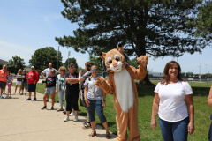 People standing in line at a school event, with a costumed mascot posing for photos.