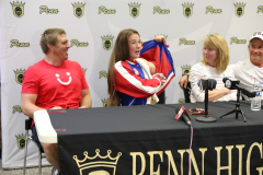 People sitting at a table in front of a microphone. A man is holding a red shirt and a woman is holding a blue shirt. They