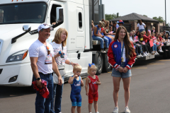 Family members posing in front of a semi truck at a parade.