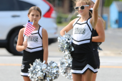 Two cheerleaders in uniforms holding American flags on a street.