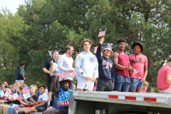 People at a parade holding flags, some are standing while others are sitting on a truck.