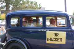 An elderly couple riding in a blue antique car during a parade.