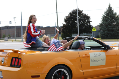 Three people sitting in a convertible car during a parade.