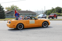 People riding in a convertible car at an outdoor event.