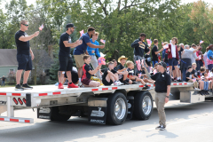 A group of people on a flatbed truck celebrating an event, with some waving flags and others holding signs.