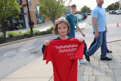 Girl holding a red shirt with white writing, standing on sidewalk.