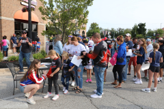 People gathered outside a restaurant, some holding signs, others standing in line, all seemingly waiting for something.