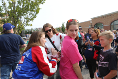 People gathered at a parade, with some looking at the camera and others engaged in conversation.