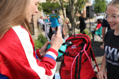 Two people standing next to a red backpack in an outdoor setting during daylight hours.
