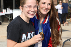 Girl in blue jacket holding a medal around her neck, posing for a picture with another person.