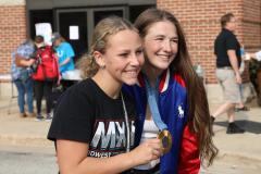 Two young women posing together at a sports event. One is wearing a medal around her neck and they are both smiling.