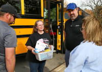 People gathered around a bus, one person holding a basket, all seemingly engaged in conversation.