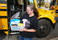 Bus driver of the month stands proudly in front of her yellow school bus, holding a basket filled with various items.