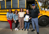 Group of people posing in front of school bus, including driver of the month.